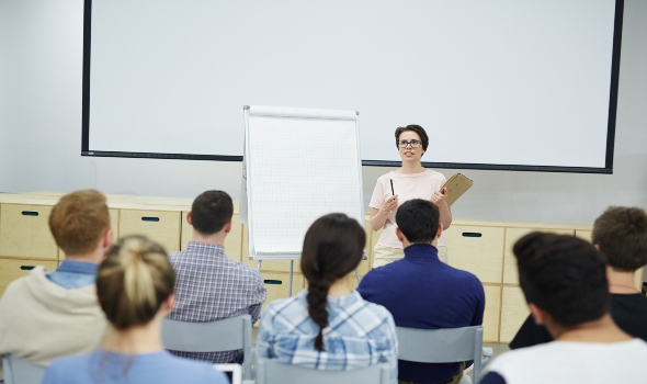 Teacher by whiteboard explaining students principles of successful business